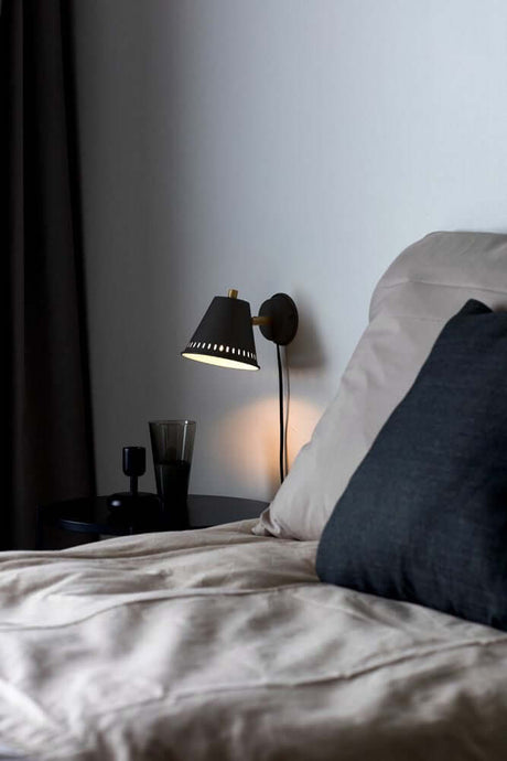 Pine wall light by a stylish bed, combined with elegant cushions and a modern bedside table.