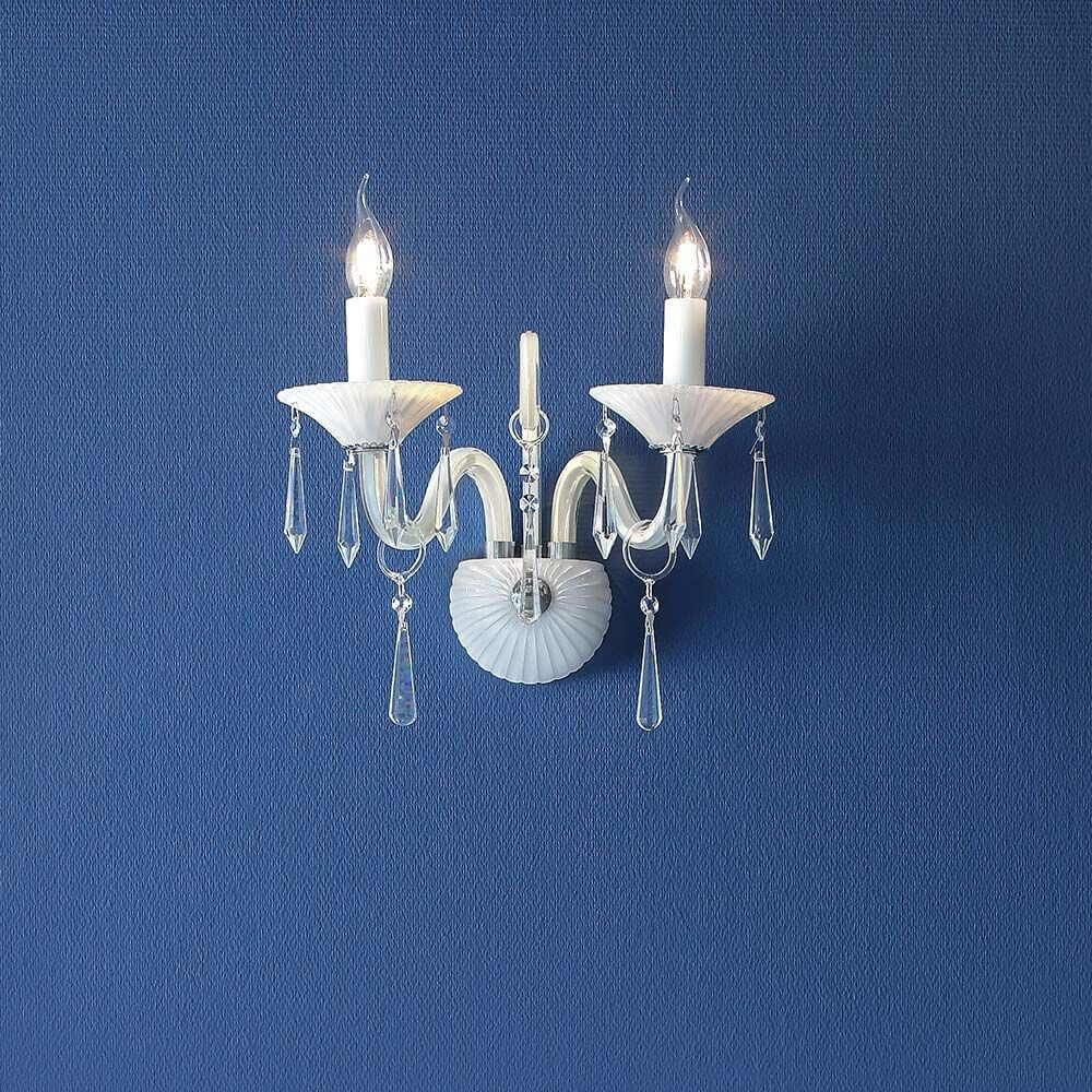Wandleuchte Rosano 2-flammig Weiß an blauer Wand mit elegantem Design und Kristallakzenten.