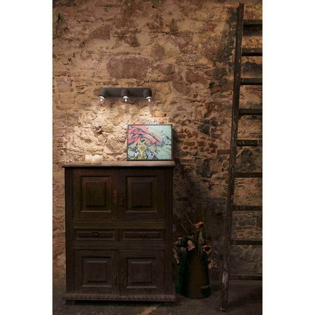 Wandstrahler STONE-3 Dunkelgrau an der Wand über einem alten Möbelstück in einem rustikalen Raum.