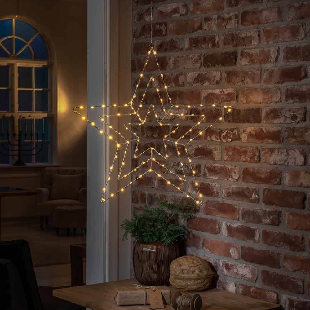 Weihnachtlicher LED Stern mit 112 Lichtpunkten IP20 an einer Ziegelmauer hängend, mit warmem Licht.