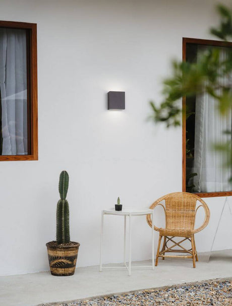 Applique extérieure Zaro LED 3000K anthracite IP65 sur un mur, entourée de plantes et d’un fauteuil de jardin.