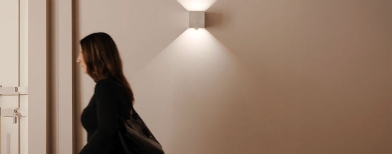 Eine Frau geht an einer Wand mit einem modernen Wandlicht vorbei.
