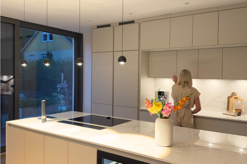 Moderne Küche mit hellem Innenraum, Frau bei der Zubereitung von Speisen und Blumen auf der Theke.