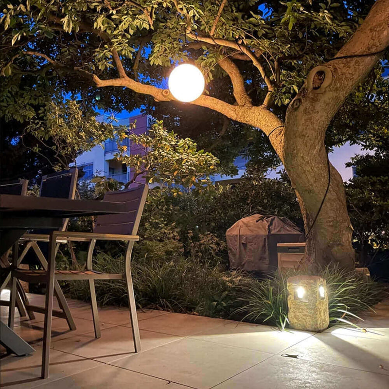 Gemütlicher Außenbereich mit einem beleuchteten Baum, Tisch und Stühlen, ideales Ambiente für entspannte Abende.