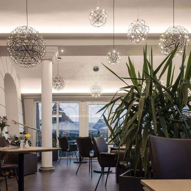 Modernes Restaurant mit stilvollen Pendelleuchten und Pflanzen, Blick auf den See durch große Fenster.