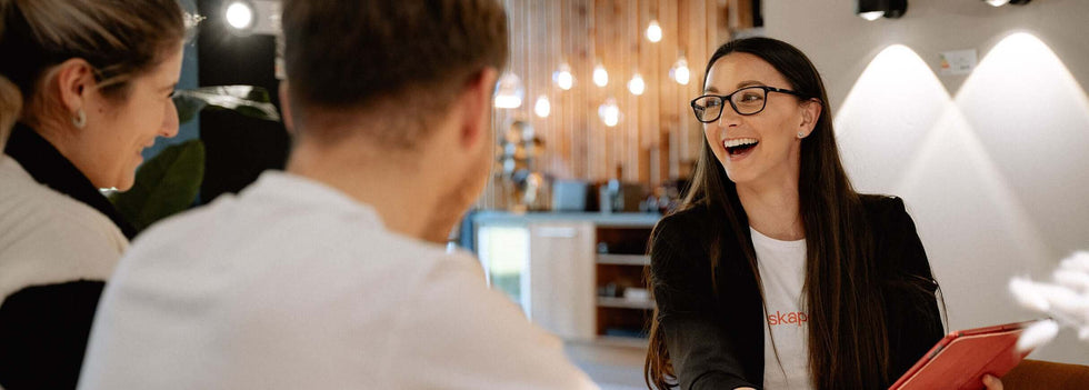 s.luce lächelt, während sie Kunden in einem modernen Café berät, mit Holzdekor im Hintergrund.