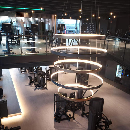 Moderne Fitnessstudio-Umgebung mit einem eleganten, hängenden Lichtdesign über den Trainingsgeräten.