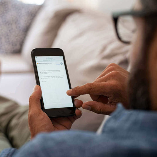 Person nutzt ein Smartphone und tippt auf dem Bildschirm, während er entspannt auf einem Sofa sitzt.