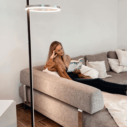 Junge Frau mit langen Haaren sitzt bequem auf einem Sofa und liest ein Buch in einem gemütlichen Raum.