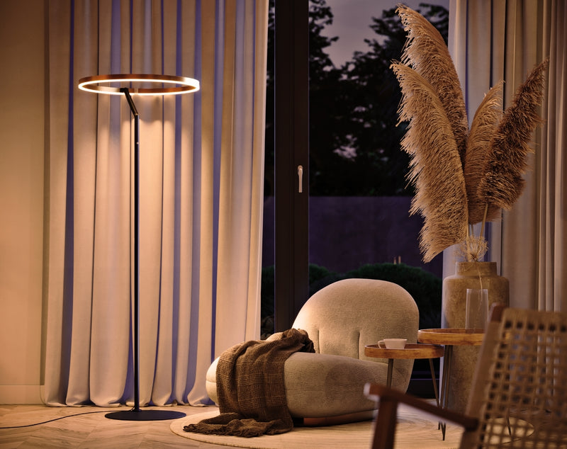 Moderne Stehlampe mit runder LED-Leuchte in einem stilvollen Wohnzimmer, umgeben von Pflanzen und gemütlichen Möbeln.