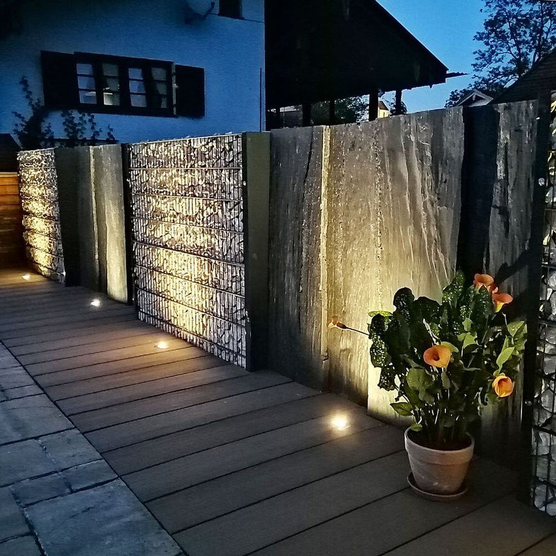 Des projecteurs encastrés de sol ronds Level en acier inoxydable IP67 éclairent une allée moderne avec des plantes.