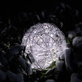 s.luce Mesh LED-Drahtkugel außen in der Nacht, umgeben von Schnee, strahlt warmweißes Licht aus.