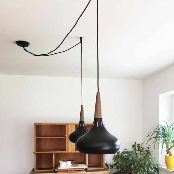 s.luce Suspensions distanciées modulaires avec deux luminaires suspendus noirs et des détails en bois dans un espace moderne.