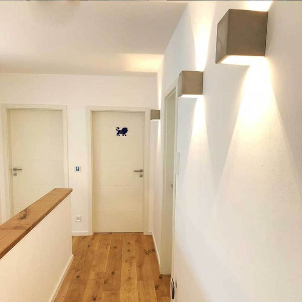 s.luce Applique Plinth in cemento grigio in un ingresso moderno con illuminazione indiretta.