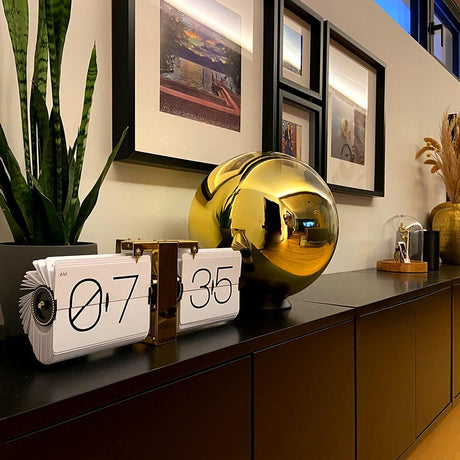 Moderne Tischdekoration mit goldener Glaskugel und analogem Wecker auf einem eleganten Sideboard.