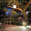 s.luce Globe Hängeleuchte leuchtet sanft in einem Garten, perfekt für stilvolle Innen- und Außeneinrichtungen.
