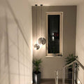 Moderne s.luce Sphere Pendelleuchte in rauchfarbenem Glas, schwebend im Treppenhaus, mit Pflanzen im Hintergrund.