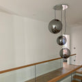 Moderne Sphere Pendelleuchte mit drei gläsernen Kugeln in rauchigem Design über einem Treppenaufgang.