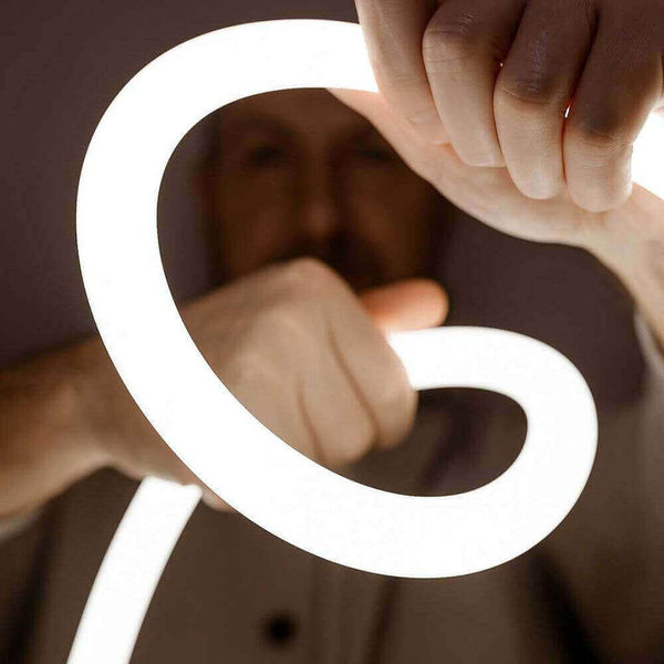 Person hält eine leuchtende, flexible Neonröhre, die in eine spiralförmige Bewegung gebogen ist.