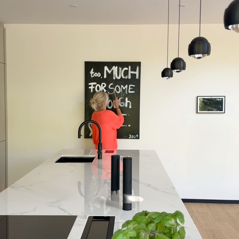 Stilvolle Küche mit Schreibtisch und moderner Dekoration, Frau schreibt auf Tafel hinter Küchentresen.