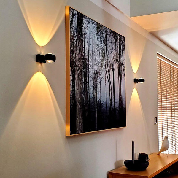 s.luce Beam Wandleuchte Up&Down mit Linsen an einer Wand, beleuchtet ein Kunstwerk mit faszinierender Lichtwirkung.