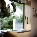 s.luce Hängelampe Crutch in moderne Einrichtung mit großem Fenster und Pflanzen im Hintergrund.