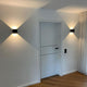 Moderne Ixa LED-Wandleuchte mit quadratischer Abdeckung an einer weißen Wand, Schattenmuster erzeugend.