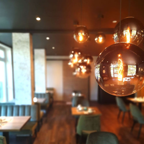 s.luce Orb Lampada a sospensione a sfera di vetro in un ambiente di ristorante elegante.