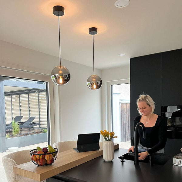 s.luce Orb Lampada a sospensione a sfera di vetro in un interno cucina moderno con una donna sorridente.