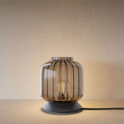 s.luce Velo Glas-Tischleuchte mit Schalter in Rauchglas auf einem Tisch, mit sichtbarem Licht.