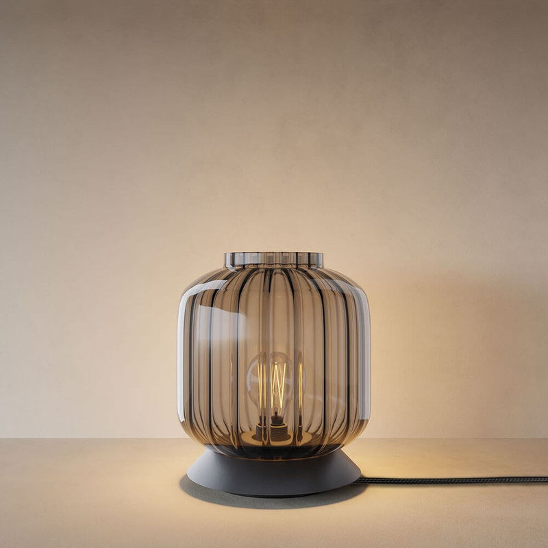 s.luce Velo Lampe de table en verre avec interrupteur en verre fumé sur une table, avec lumière visible.