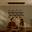 s.luce Velo Esstischlampe 12-flammig 200cm 3-reihig Ø 20cm über einem stilvollen Esstisch mit Personen.