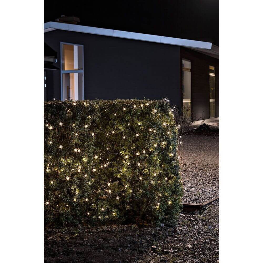 LED Lichterkette Lichtsensor Timer 240 Warmweiße Dioden batteriebetrieben IP44 an einem begrünten Zaun im Dunkeln.