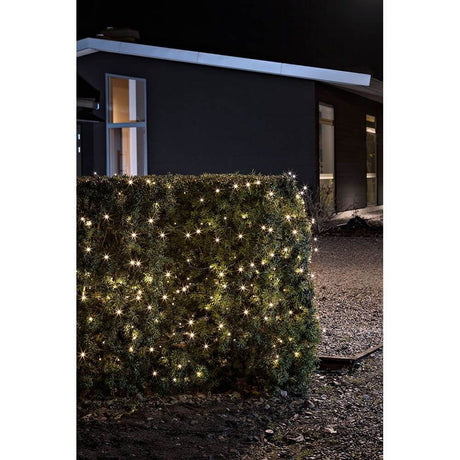 LED string of lights light sensor timer 240 warm white diodes battery-operated IP44 on a green fence in the dark.
