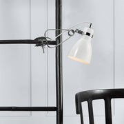 Cyclone klämspotlight vit på en hylla ovanför en svart stol, modern och tidlös design.