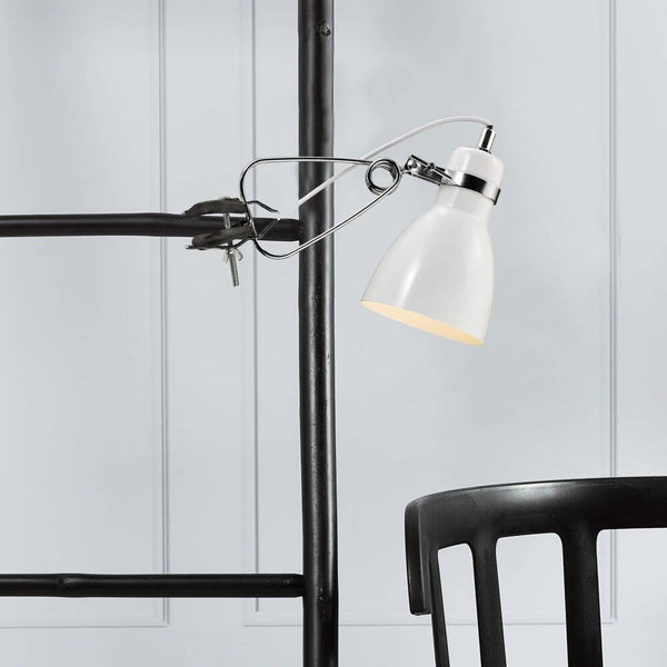 Pince lumineuse Cyclone blanche sur une étagère au-dessus d’une chaise noire, design moderne et intemporel.