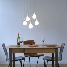 Sospensione a 5 luci Drop-2XS LED Liquid-Light bianca sopra un tavolo con vino e bicchieri.