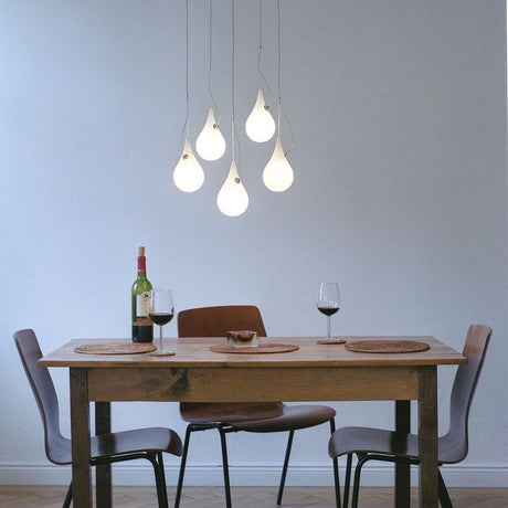 Sospensione a 5 luci Drop-2XS LED Liquid-Light bianca sopra un tavolo con vino e bicchieri.