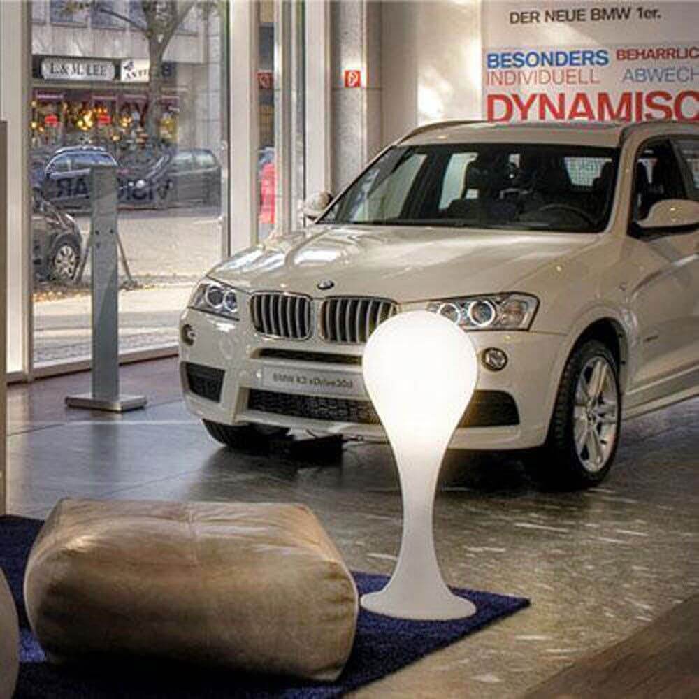 Drop-4L Outdoor Stehleuchte 100cm IP44 Liquid-Light Weiß neben einem BMW X3 in einem modernen Ausstellungsraum.